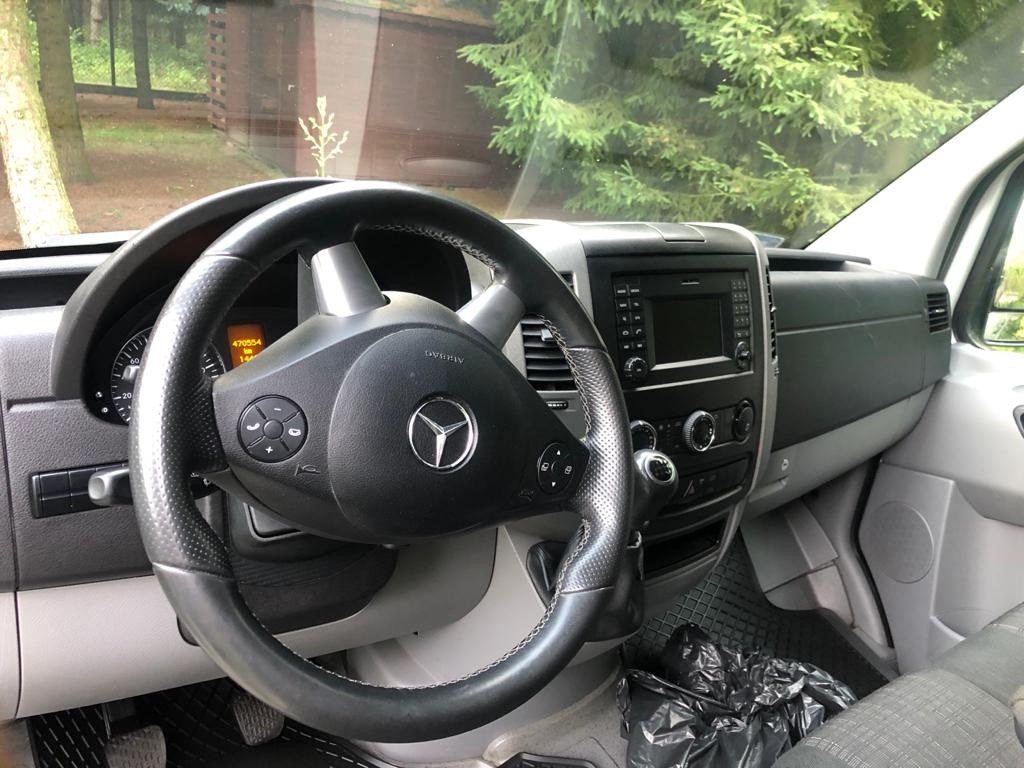 Wnętrze kabiny kierowcy busa Mercedes-Benz z widoczną kierownicą z logo, deską rozdzielczą i czarnym workiem na podłodze.