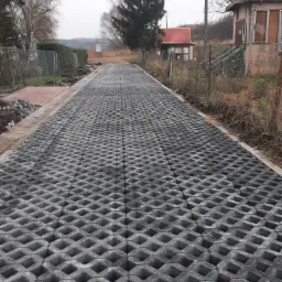 Ułożona nawierzchnia z ażurowych płyt betonowych na drodze wiejskiej w pochmurny dzień, widoczne ślady ziemi i niedokończone obrzeża.