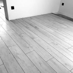 Usługi remontowo wykończeniowe - Ułożone jasne panele podłogowe w pokoju z białymi ścianami i czarnymi gniazdkami elektrycznymi, widoczne lekkie zabrudzenia na podłodze.