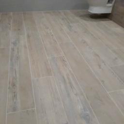 Usługi remontowo wykończeniowe - Jasne, podłużne płytki imitujące drewno na podłodze w łazience z podwieszaną toaletą.