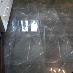 Usługi remontowo wykończeniowe - Błyszcząca, ciemnoszara podłoga z płytek imitujących marmur, ułożona w dużej łazience z białymi szafkami i grzejnikiem drabinkowym.