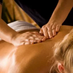 Kobieta leży na brzuchu, otrzymując masaż pleców; widoczne dłonie masażysty i fragment włosów kobiety spiętych w kucyk.