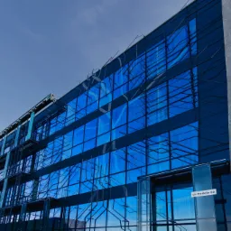 Nowoczesny budynek biurowy z fasadą z niebieskiego szkła i metalu, adres ul. Podole 60 widoczny na szklanym panelu przy wejściu.