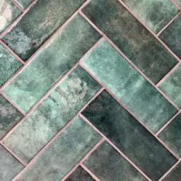 Ułożone w jodełkę, szkliwione, prostokątne płytki w odcieniach zieleni z różową fugą.