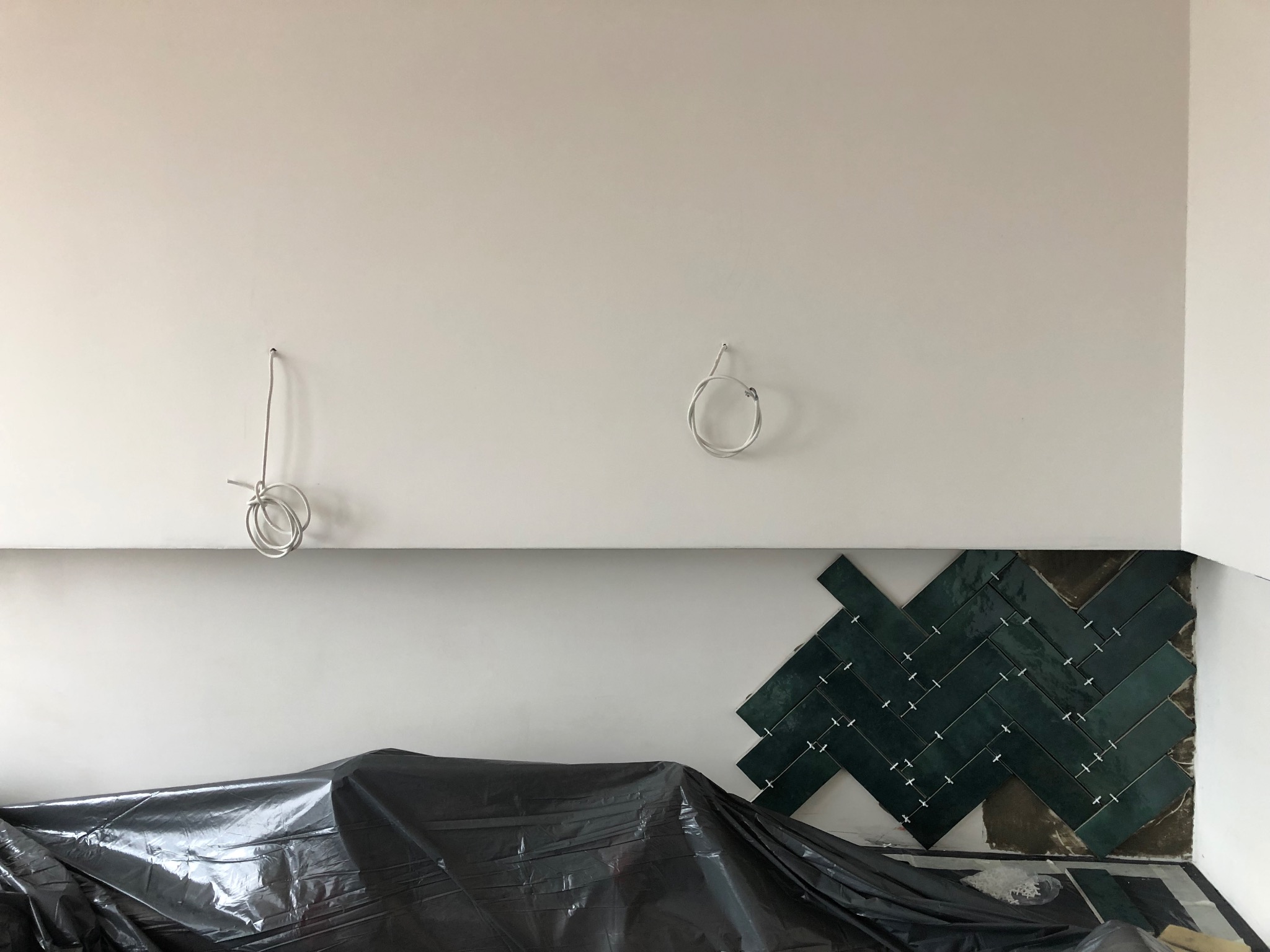 Montaż ciemnozielonych płytek w jodełkę na ścianie, częściowo zakrytych folią ochronną, z widocznymi przewodami elektrycznymi na górze ściany.