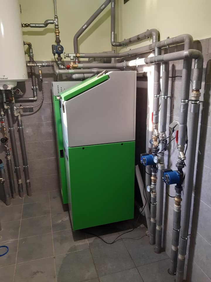 Nowoczesny, zielono-szary piec CO w kotłowni w Zduńskiej Woli, z licznymi rurami i zaworami, zainstalowany na szarej, kafelkowej podłodze.