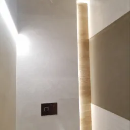 Nowoczesna łazienka z ukrytym oświetleniem LED, drewnopodobna okładzina ścienna i minimalistyczny przycisk spłuczki w zabudowie podtynkowej.