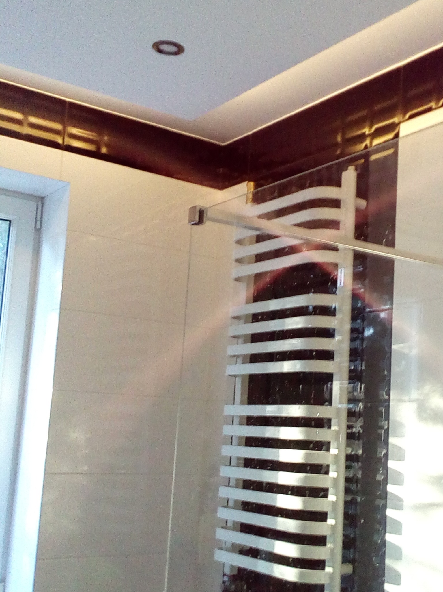 Wykończona łazienka z białymi płytkami, brązową dekoracyjną listwą pod sufitem i grzejnikiem drabinkowym w kolorze białym.