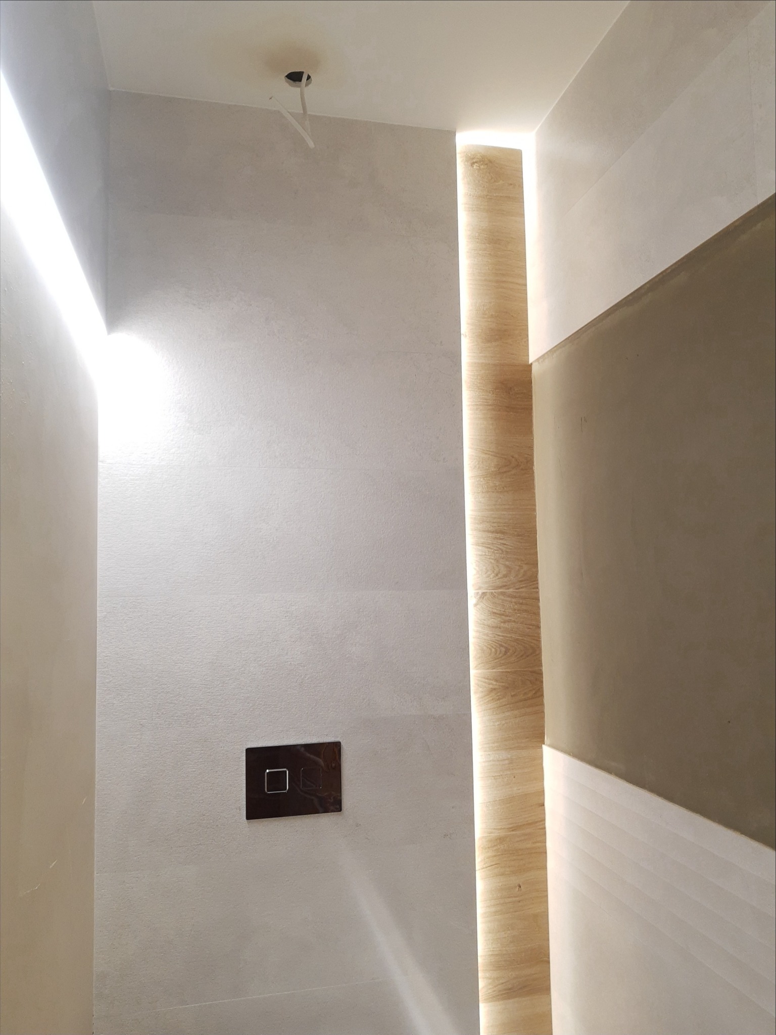 Nowoczesna łazienka z ukrytym oświetleniem LED, drewnopodobna okładzina ścienna i minimalistyczny przycisk spłuczki w zabudowie podtynkowej.