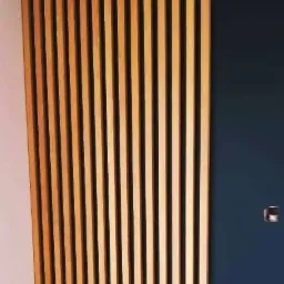 Drewniane lamele pionowe na ścianie, część ściany pomalowana na granatowo, widoczne gniazdka elektryczne.