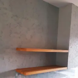 Dwie drewniane p&oacute;łki zamontowane na szarej ścianie z dekoracyjnym tynkiem w Tropach Elbląskich.