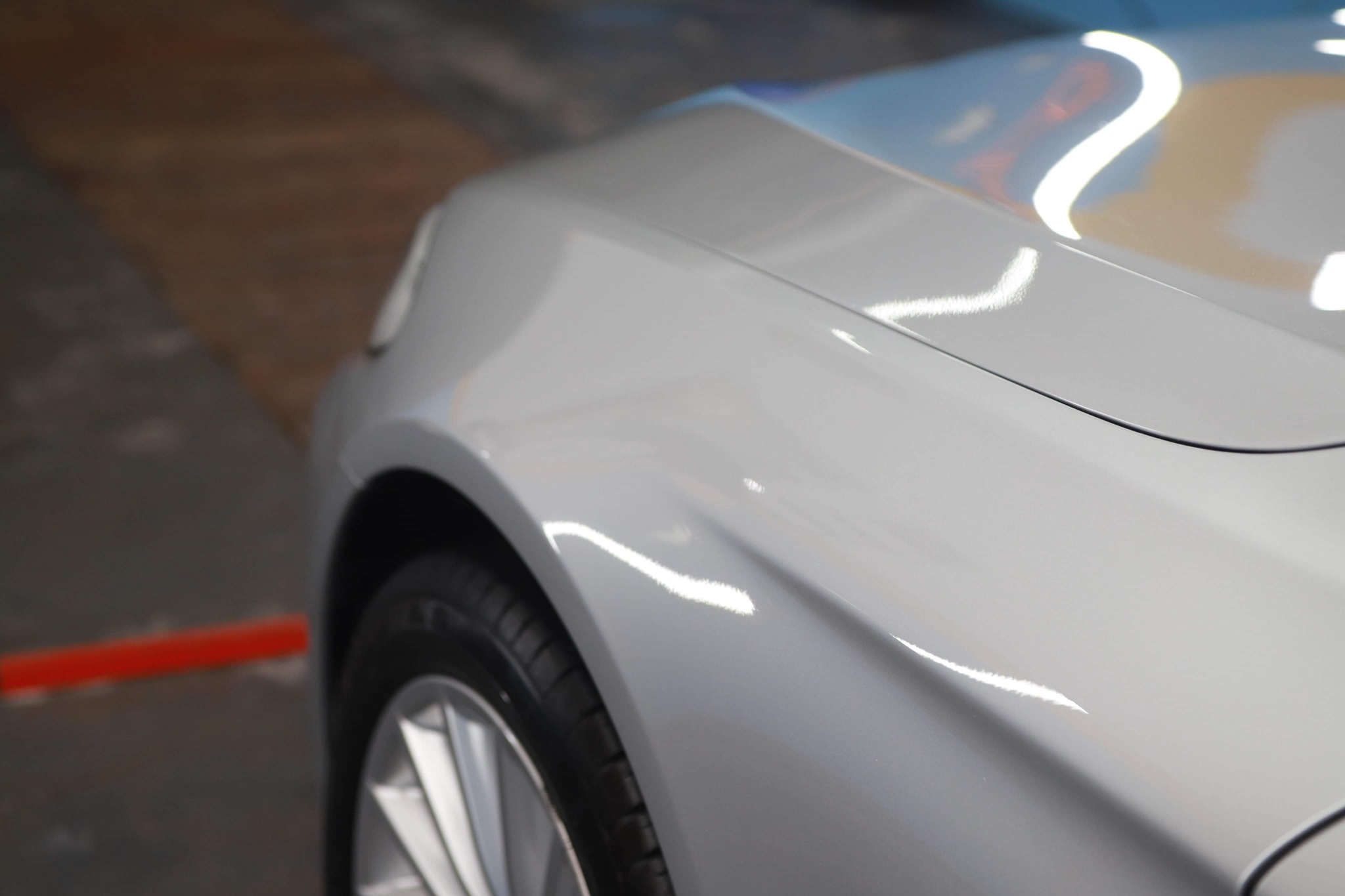 Fragment karoserii srebrnego samochodu po umyciu z widocznymi odbiciami światła, koło z aluminiową felgą, Białystok.