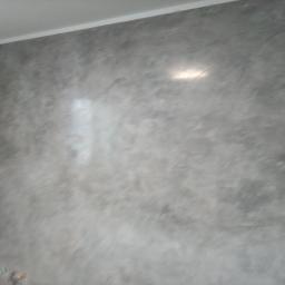 Jacek Zgraja - Ściana pokryta szarą, dekoracyjną gładzią z efektem chmur, widoczne refleksy światła.