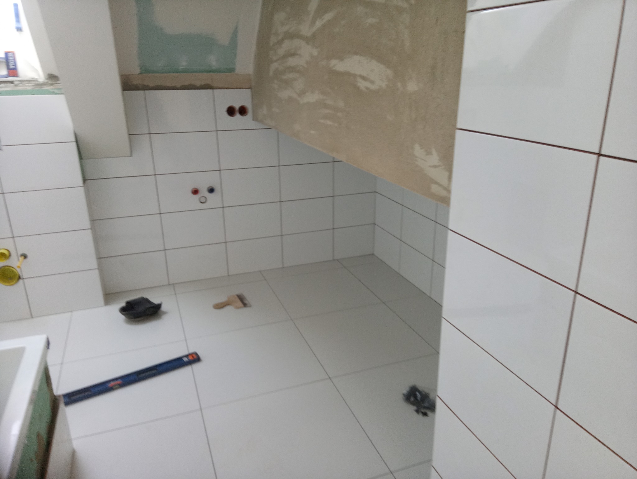 Wnętrze kuchni w trakcie układania białych płytek z ciemnymi fugami w Krakowie, widoczne narzędzia glazurnicze i fragmenty niezabezpieczonych ścian.