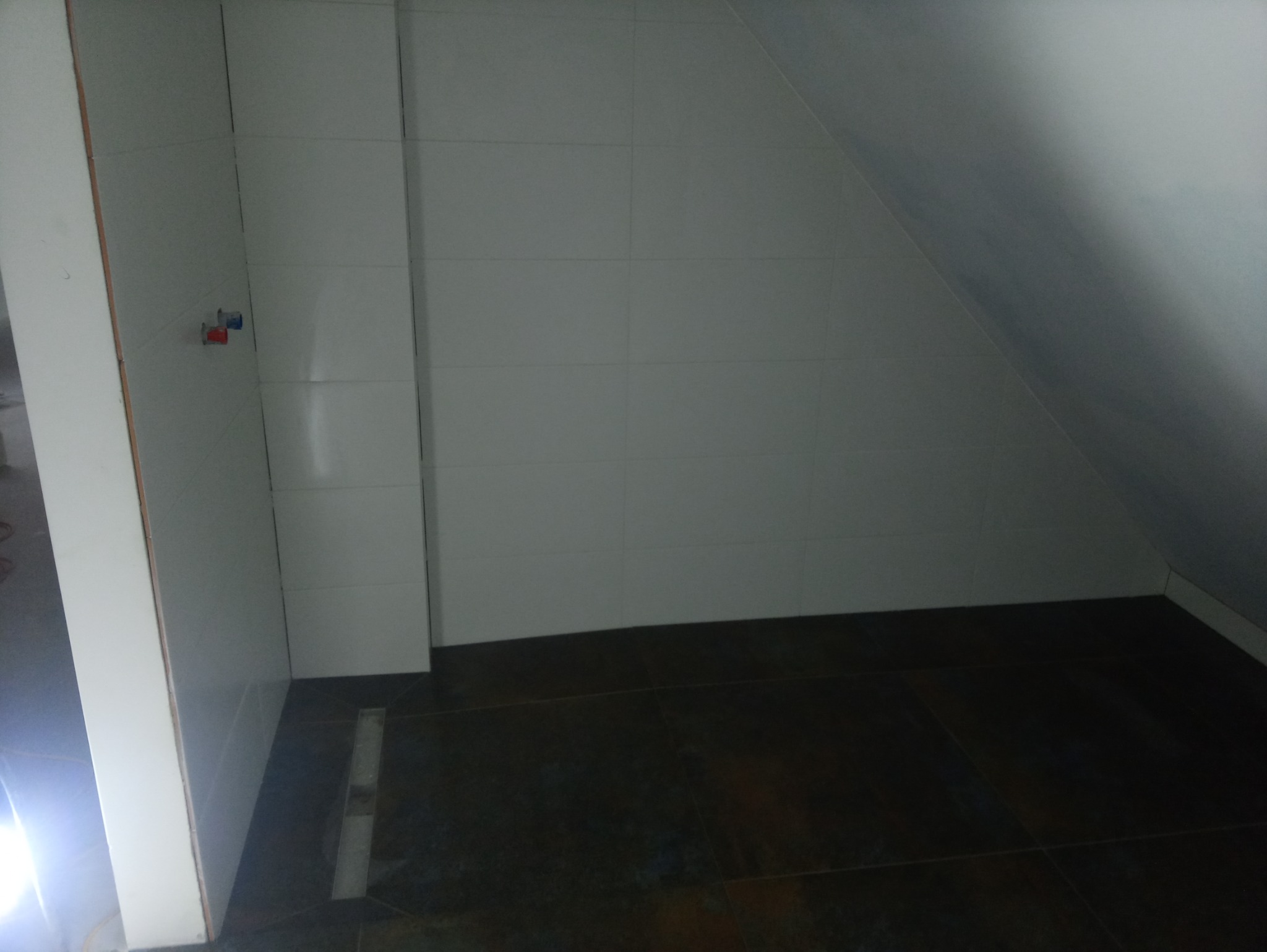 Ukończona łazienka na poddaszu z białymi płytkami ściennymi, ciemną podłogą i odpływem liniowym w podłodze.