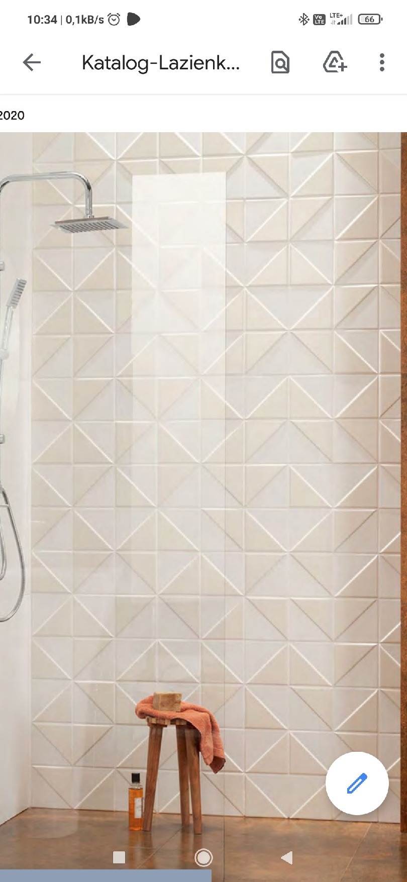 Kabina prysznicowa z geometryczną, trójwymiarową glazurą w odcieniach bieli, uzupełniona o drewniany stołek z ręcznikiem i butelką kosmetyku, całość w jasnym świetle.