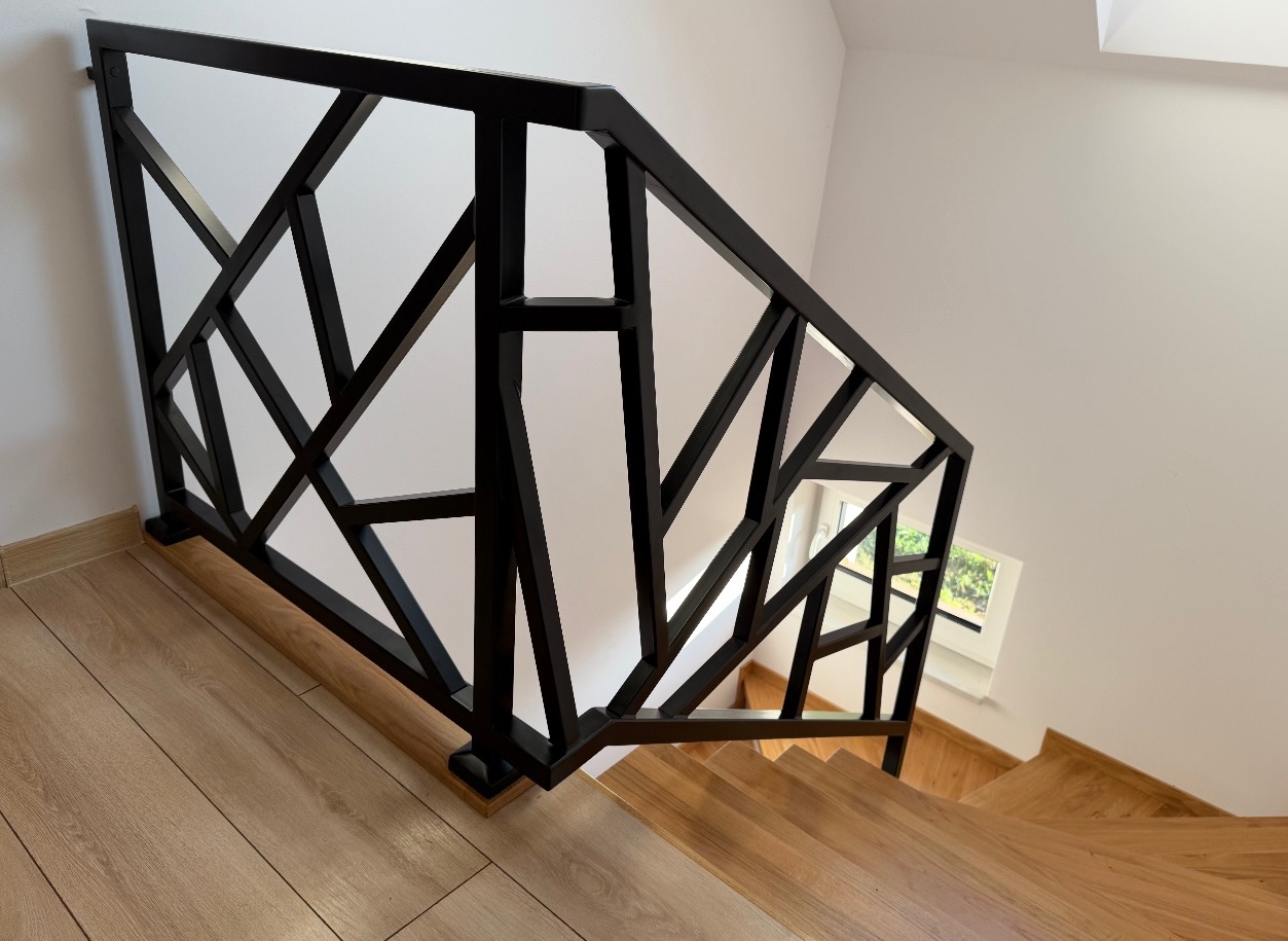 Nowoczesna, geometryczna balustrada schodowa w kolorze czarnym, wykonana w Perle. Widok z góry na drewniane schody i fragment okna.