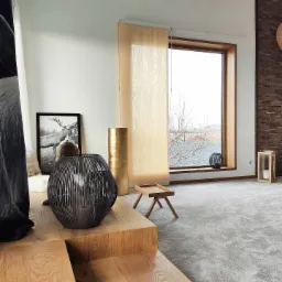 Nowoczesna sypialnia w neutralnych kolorach z drewnianymi akcentami, dekoracyjną lampą w kształcie kuli i obrazem jelenia w czarnej ramie, widok na zewnątrz przez duże okno z jasną zasłoną panelową.