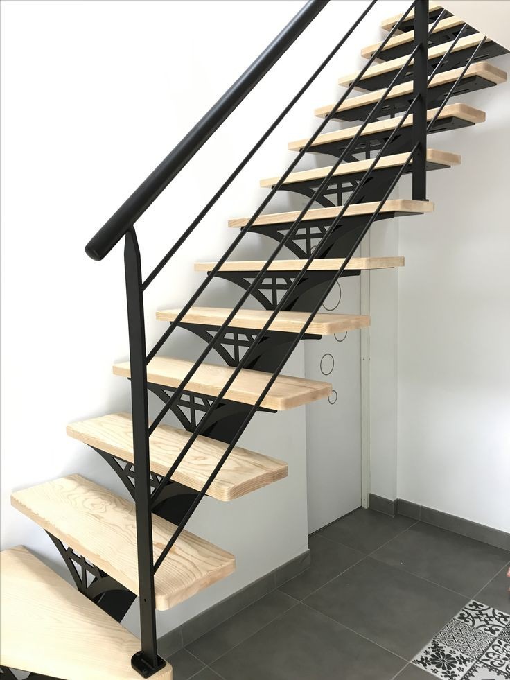 Nowoczesne schody z drewnianymi stopniami i czarną metalową konstrukcją wspornikową, widoczne z boku na tle białej ściany i szarej podłogi.