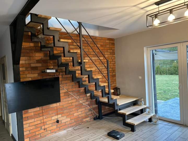 Nowoczesne schody metalowe z drewnianymi stopniami na tle ściany z czerwonej cegły w jasnym wnętrzu domu.