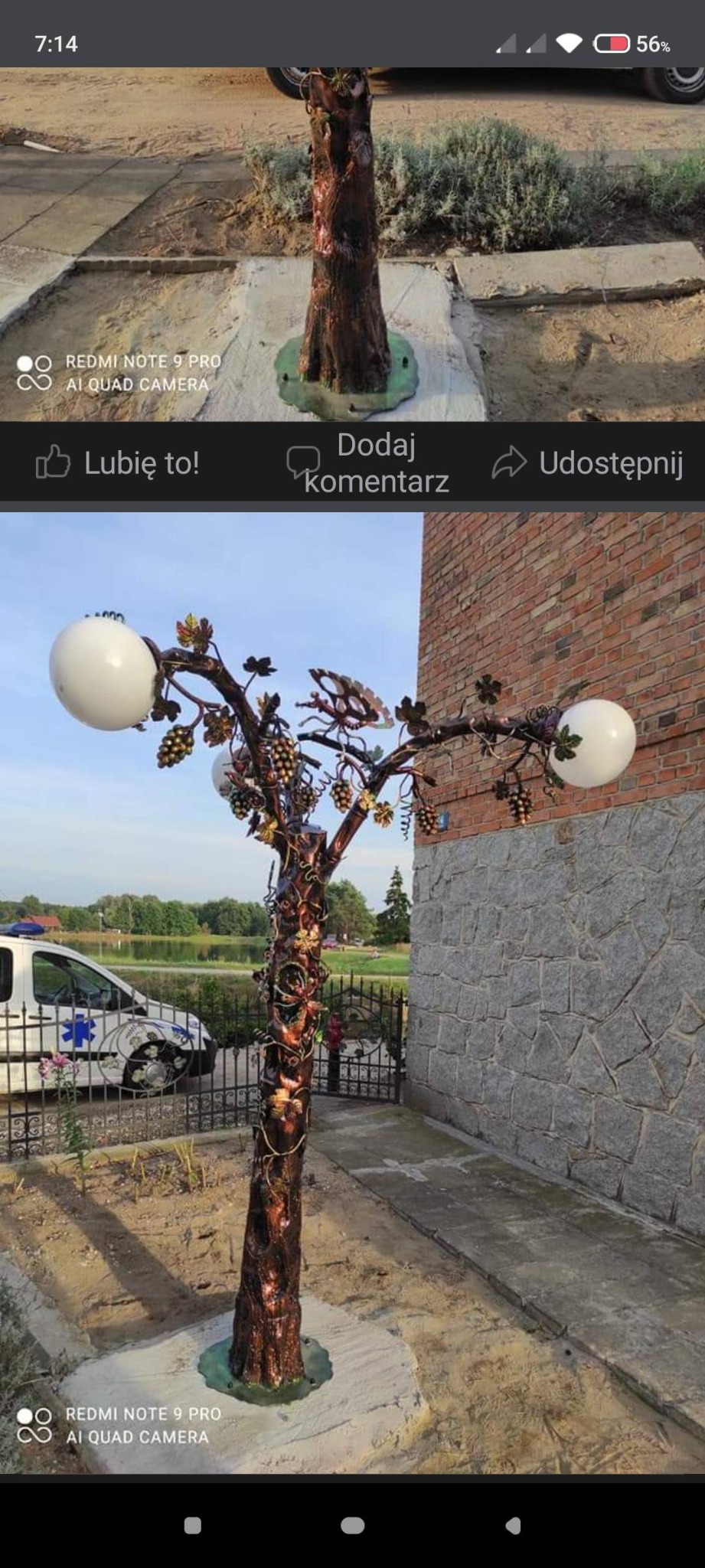 Kuta metalowa lampa ogrodowa w kształcie drzewa z dekoracjami winogron i kulistymi kloszami, umieszczona przed budynkiem z kamienną elewacją i ogrodzeniem.