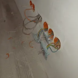 Ściana w trakcie remontu z widocznymi puszkami instalacyjnymi, wystającymi przewodami i zamontowanymi puszkami pod gniazdka, na podłodze resztki gruzu i farby.