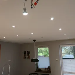 Sufit z zamontowanymi punktowymi lampami LED, widoczna również lampa wisząca i tymczasowa lampa robocza podwieszona na przewodach.