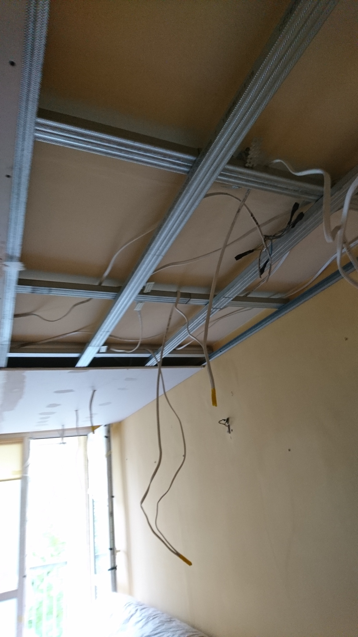 Montaż sufitu podwieszanego z widocznymi przewodami elektrycznymi i metalową konstrukcją nośną w trakcie prac.