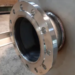 Spawana, nierdzewna flansza z otworami na śruby, przymocowana do metalowej rury, widoczne ślady spawania.