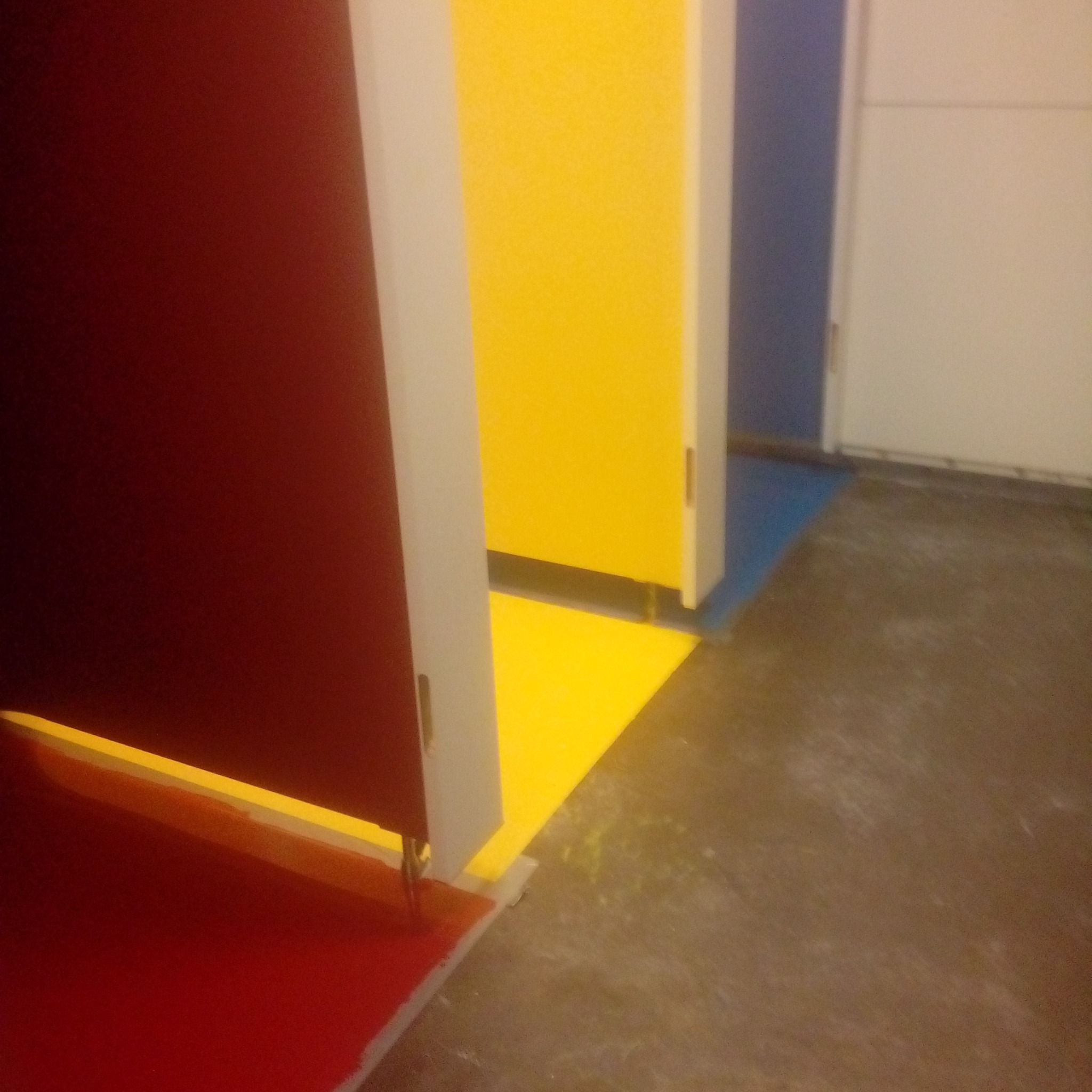 Wielokolorowe kabiny toaletowe z posadzką z żywicy w odcieniach czerwieni, żółci i niebieskiego, widoczne z perspektywy podłogi, z niedoskonałościami na powierzchni.