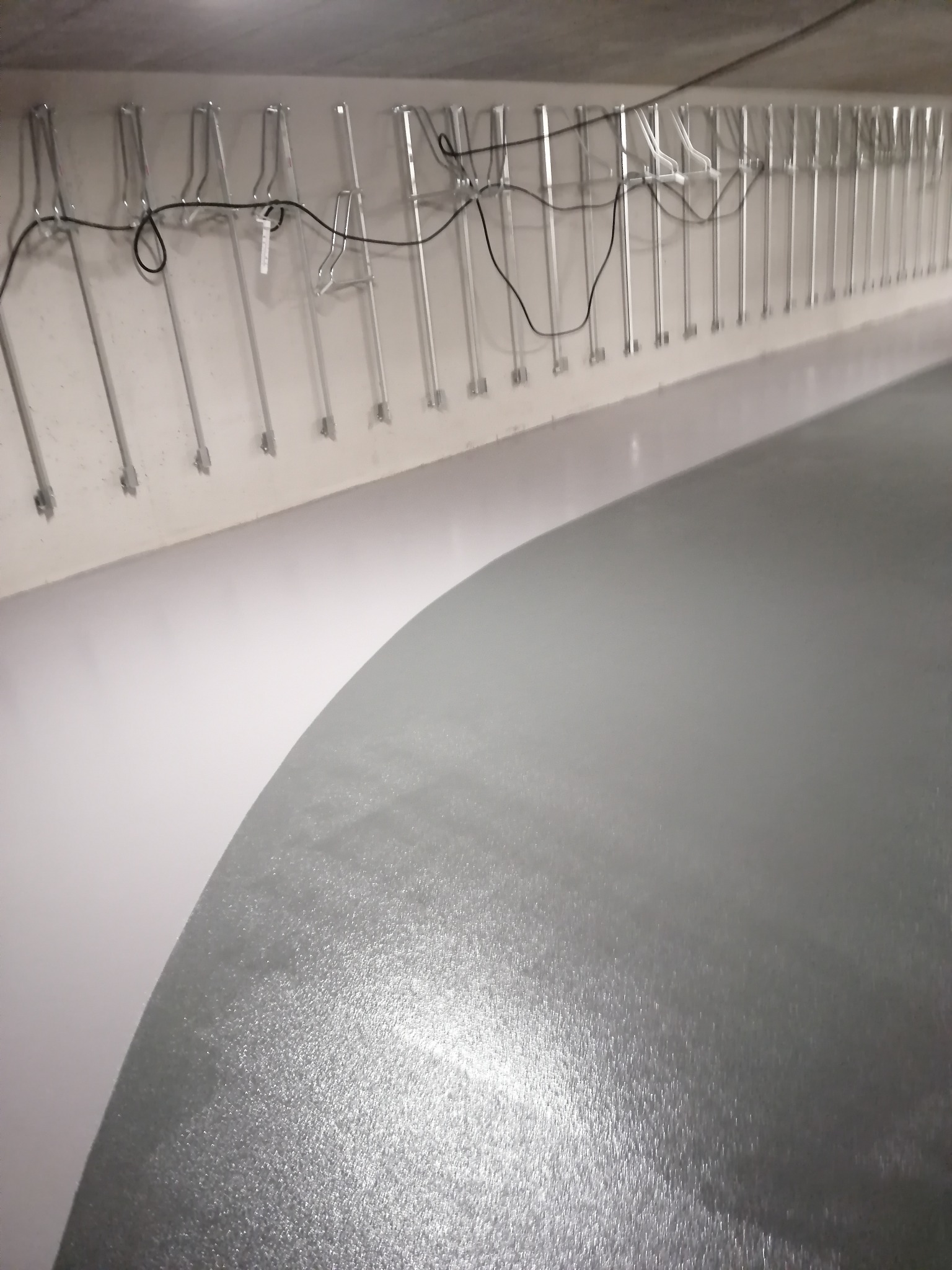 Szara, błyszcząca posadzka w garażu podziemnym z metalowymi wieszakami na rowery przymocowanymi do ściany nad nią.