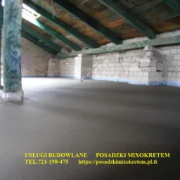 Gładka, szara wylewka na poddaszu z drewnianą konstrukcją dachu i fragmentami muru z białej cegły. Widoczne zabezpieczenie ścian folią. Świeżo wykonana posadzka.