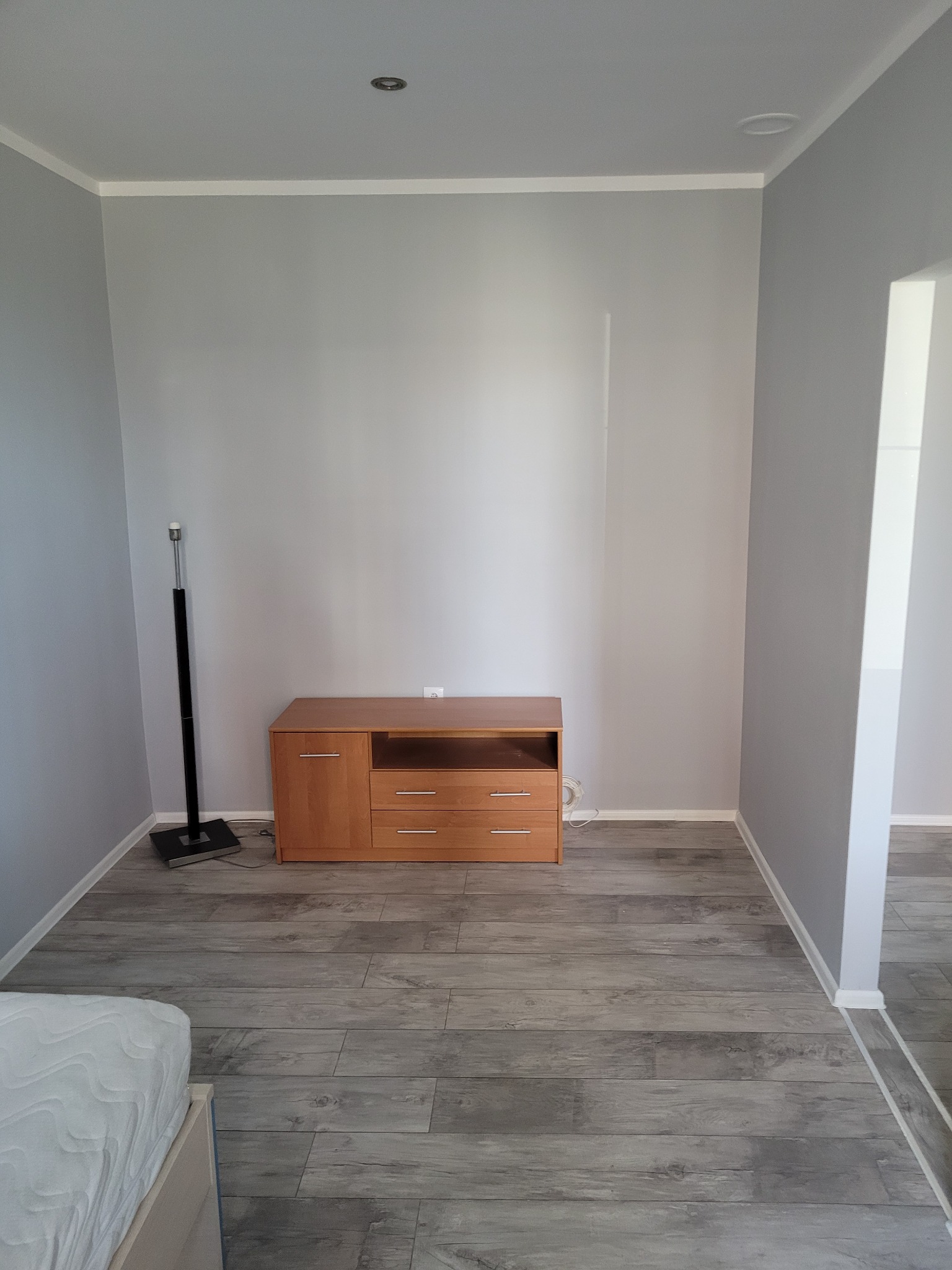 Szare ściany w pokoju po remoncie, drewniana komoda, panele podłogowe imitujące drewno, listwy przypodłogowe.