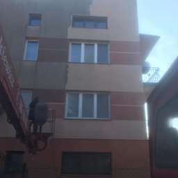 Agnes-Bud Agnieszka Figarska - Pracownicy na podnośniku koszowym czyszczą fragment fasady budynku wielorodzinnego, widoczna wyraźna różnica między umytą a zabrudzoną powierzchnią.