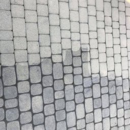 Agnes-Bud Agnieszka Figarska - Ułożona szara kostka brukowa, widoczna różnica w odcieniach na części powierzchni, sugerująca etap czyszczenia lub wilgotną plamę.