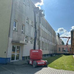 Agnes-Bud Agnieszka Figarska - Częściowo umyta elewacja budynku z podnośnika Manitou. Na drugim planie kolejny podnośnik. Widoczne okna i trawnik. Słoneczny dzień.