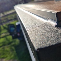 DeBest Wykończenia Wnętrz Remonty - Detale wykończenia nowej zabudowy balkonu z widokiem na zieleń i fragment budynku w tle, oświetlone jasnym słońcem.