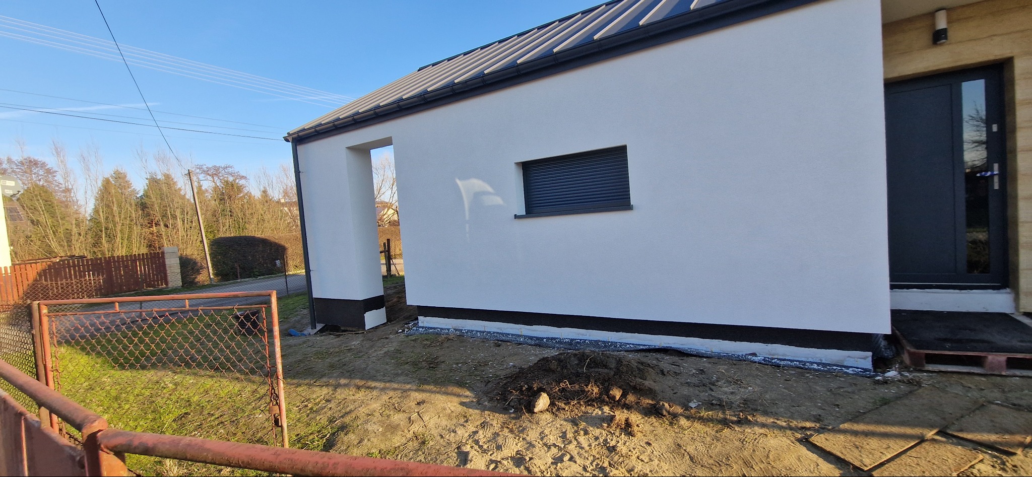 Nowo otynkowany budynek z grafitową stolarką okienną i drzwiową, widok z zewnątrz, świeżo uporządkowany teren wokół budynku.