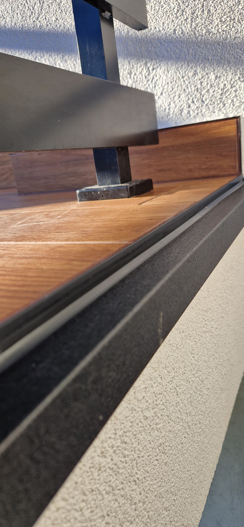 Szczegółowe ujęcie zabudowy balkonu z drewnopodobną podłogą, czarną ramą i oświetloną fakturą ściany.