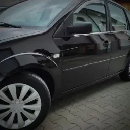 Błyszczący czarny samochód osobowy zaparkowany na szarej kostce brukowej, widoczne odbicia w lakierze i srebrne felgi.