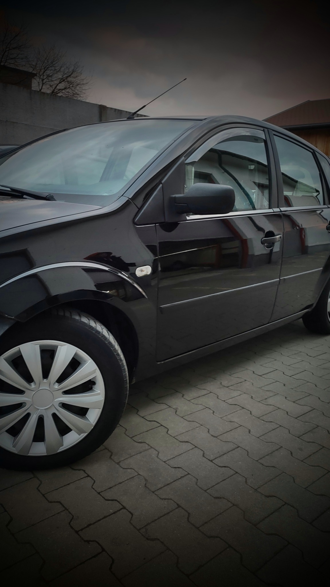 Błyszczący czarny samochód osobowy zaparkowany na szarej kostce brukowej, widoczne odbicia w lakierze i srebrne felgi.