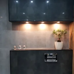 Nowoczesna łazienka z podświetlanymi szafkami w kolorze grafitowym, dekoracyjnymi figurkami mnichów i bonsai w białej doniczce.