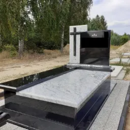 Nowoczesny nagrobek z jasnego i czarnego kamienia, z wygrawerowanym napisem 'Jezu Ufam Tobie' i krzyżem, na tle drzew.