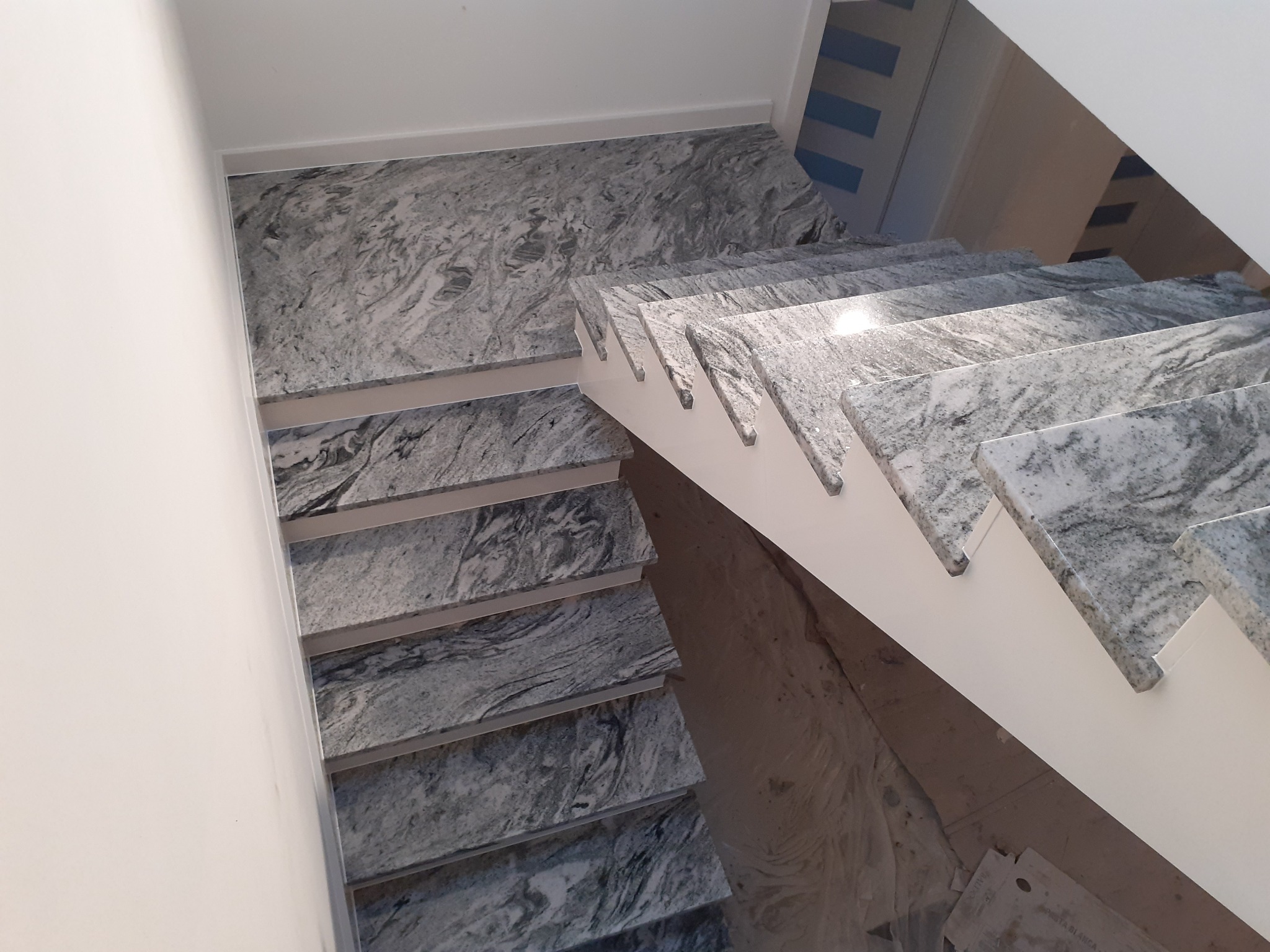 Wewnętrzne schody z szarego kamienia z białymi podstopnicami, widok z góry na dół, z widoczną fakturą kamienia.