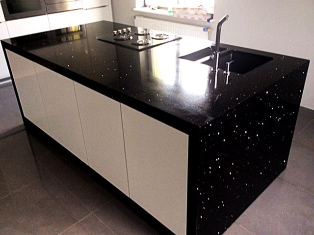 Czarny, błyszczący blat kuchenny z wbudowanym zlewem i płytą grzewczą, osadzony na białych szafkach w nowoczesnej kuchni.