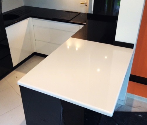 Biały, gładki blat kuchenny z zaokrąglonym rogiem, kontrastujący z czarnymi szafkami i blatem w tle, w nowoczesnej kuchni.