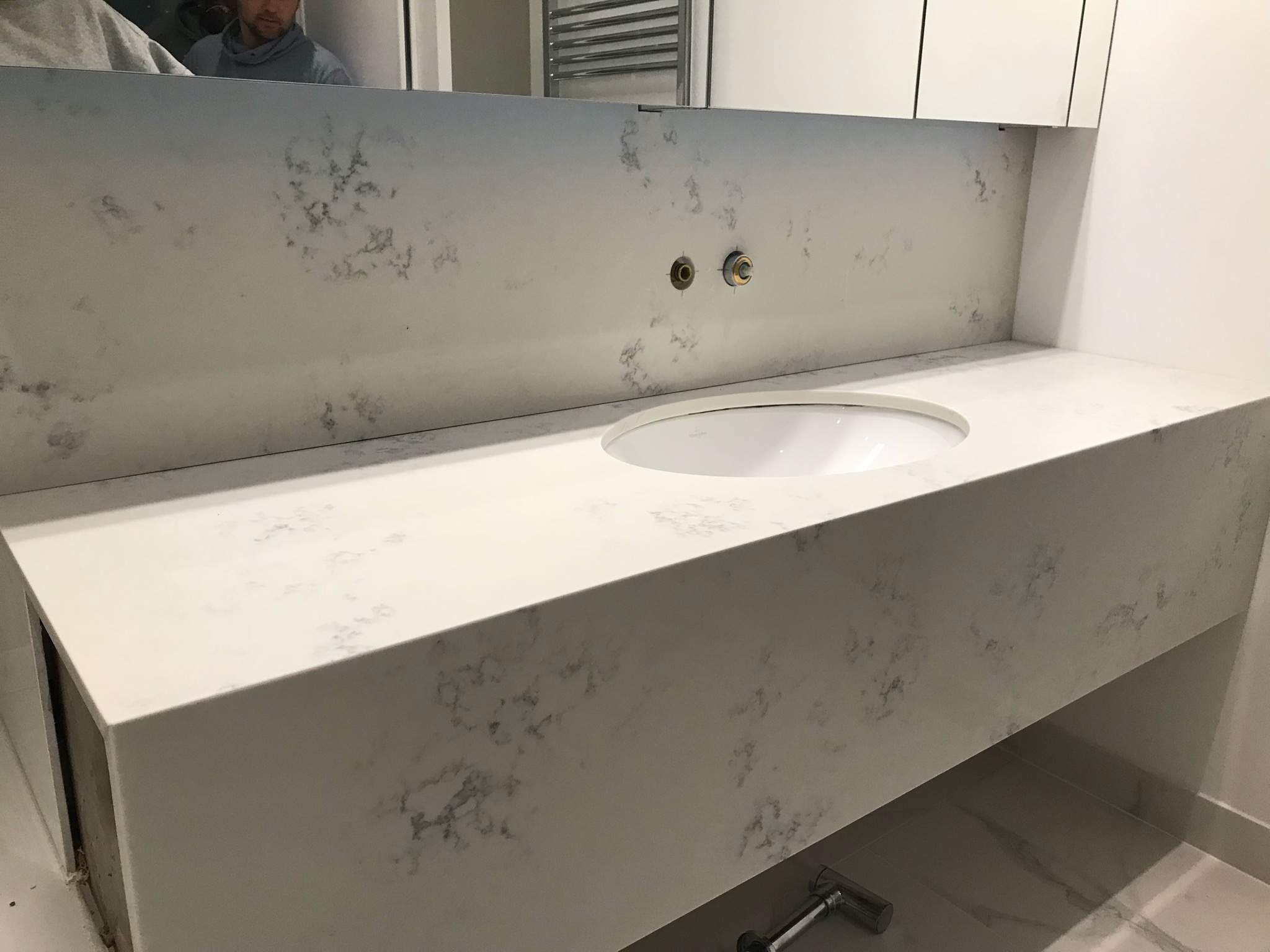 Łazienka z blatem z konglomeratu Carrara i wpuszczaną umywalką Villeroy & Boch, widoczne przygotowane przyłącza do baterii.