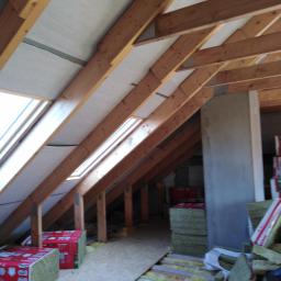 Onsetbud Zhanna Slyvka - Poddasze w trakcie prac: drewniana konstrukcja dachu z oknami, częściowo ocieplona wełną mineralną, widoczne płyty OSB i opakowania wełny.