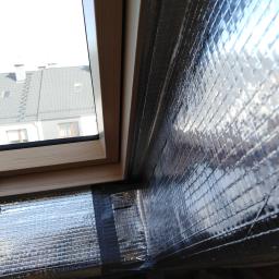 Onsetbud Zhanna Slyvka - Poddasze z oknem dachowym w trakcie ocieplania, widoczna srebrna folia izolacyjna z siatką, zabezpieczona czarną taśmą. W tle dach sąsiedniego budynku.