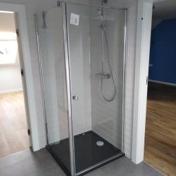 Onsetbud Zhanna Slyvka - Kabina prysznicowa z czarnym brodzikiem i chromowaną armaturą, zamontowana w łazience z szarymi płytkami podłogowymi i białymi panelami ściennymi, widok na otwarte drzwi do sąsiednich pomieszczeń...